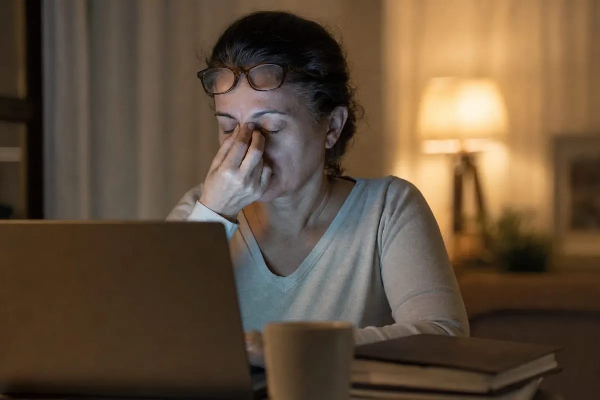 Mujer de unos 50 años trabajando de noche con dos pantallas en el escritorio